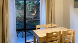 A dining area with a table and chairs, a glass door leading to an outdoor area with greenery, and an air conditioning unit on the wall. - Royal Park Lodge (Auckland)