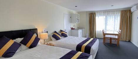 Ein Hotelzimmer mit zwei Betten, einem Schreibtisch, einem Stuhl, einer kleinen Küchenzeile und einem Fenster mit Vorhängen.