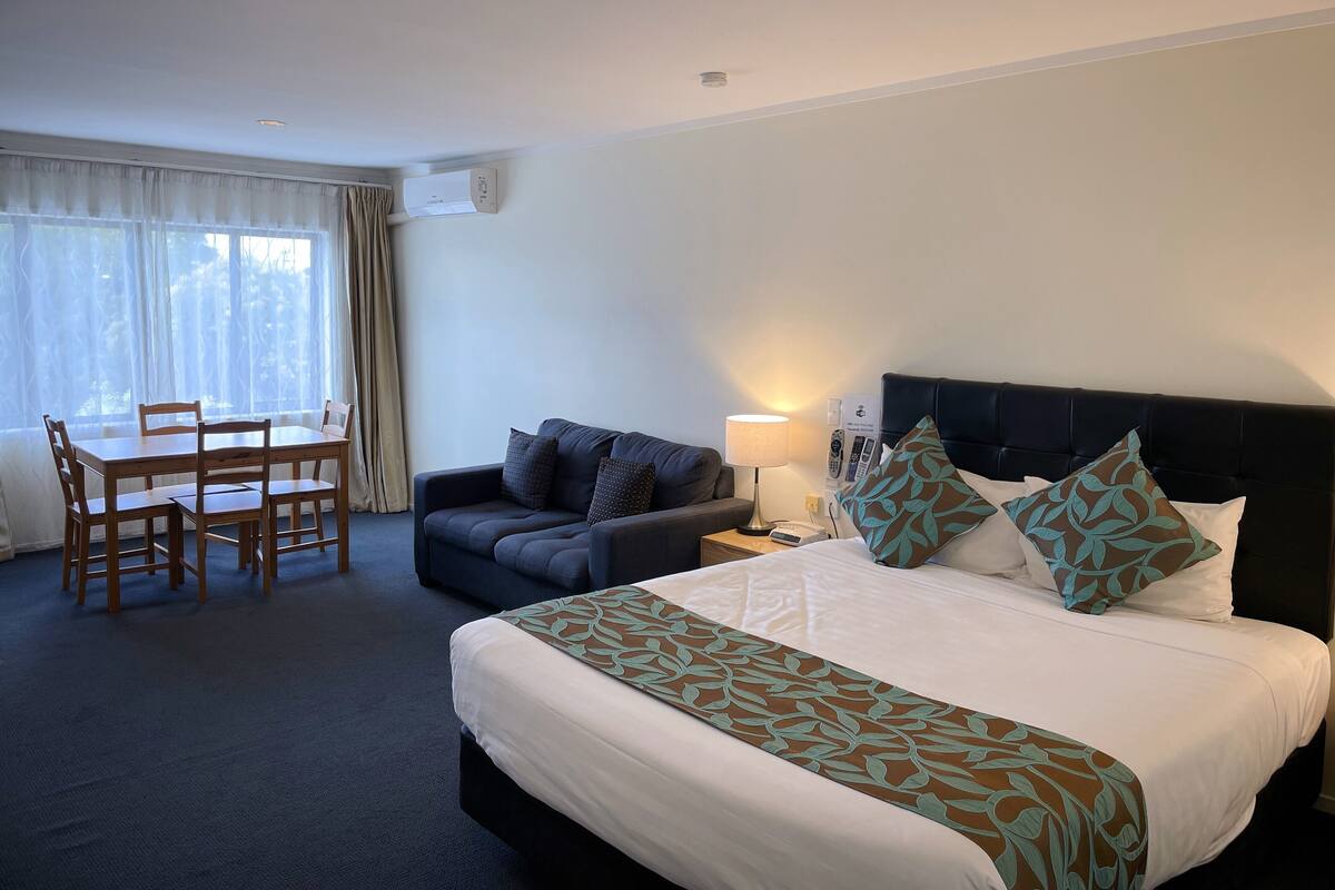 A hotel room with a bed, a sofa, a dining table, and a lamp.