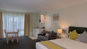 A hotel room with a bed, a sofa, a dining table, and a kitchenette. - Royal Park Lodge (Auckland)