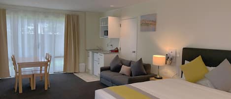 A hotel room with a bed, a sofa, a dining table, and a kitchenette.