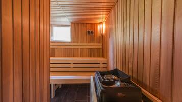 Una sauna con paredes y bancos de madera, una ventana y un calentador de sauna sobre una mesa.