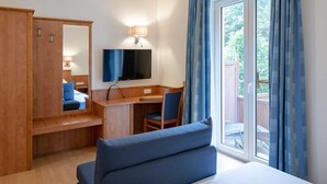 Ein Hotelzimmer mit einem Bett, einem Schreibtisch mit Stuhl, einem Fernseher und einem großen Fenster mit Vorhängen.