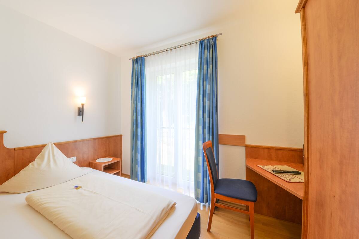 Een hotelkamer met een bed, een bureau, een stoel, een nachtkastje en een wandlamp.