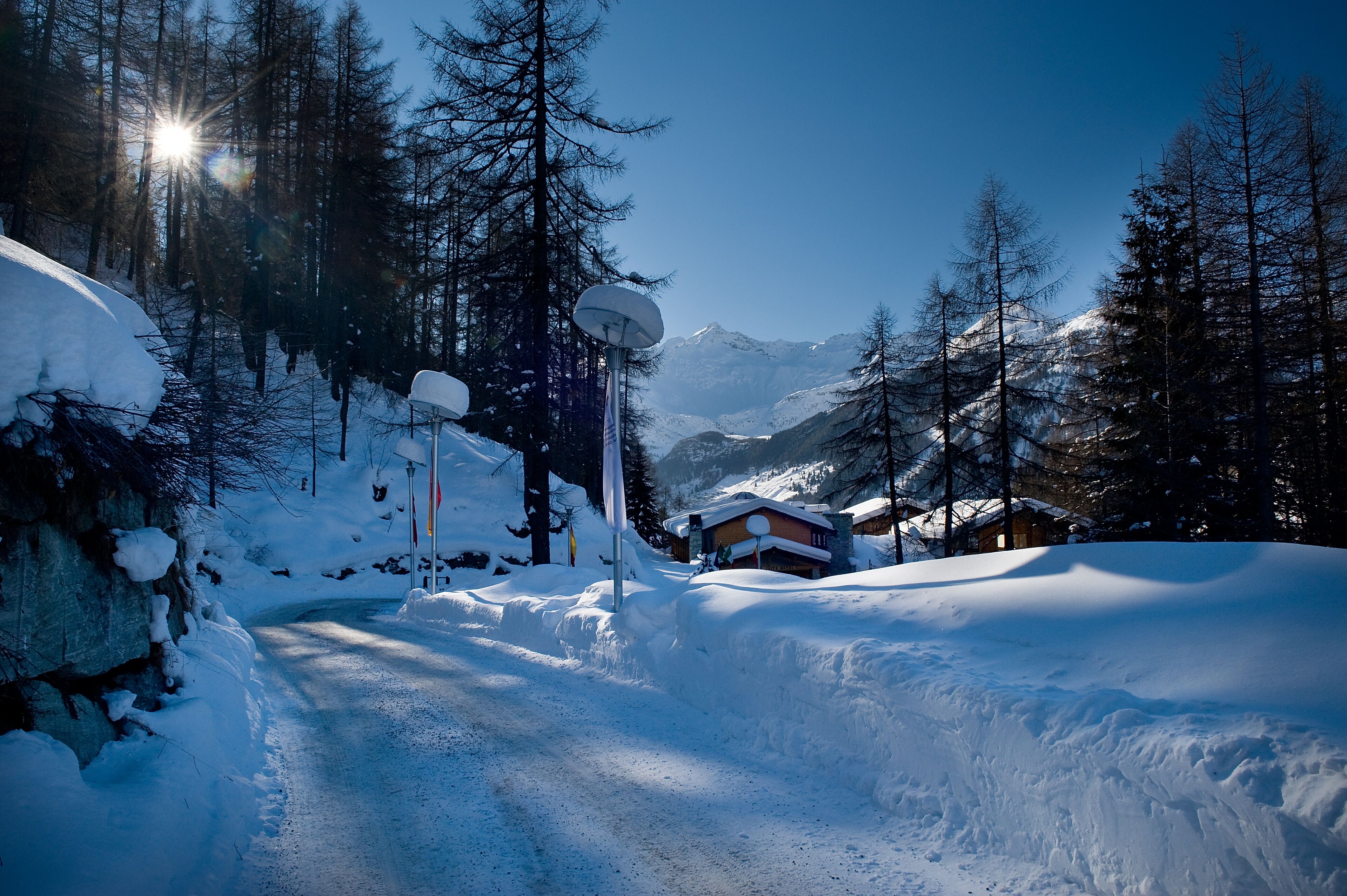 Eine verschneite Straße mit einer Holzhütte und einem Berg im Hintergrund.
