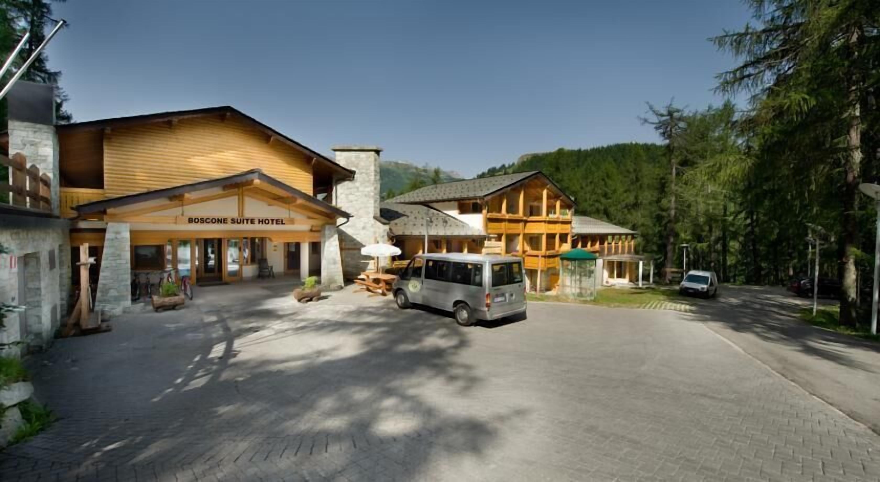 Ein Hotel mit Holzfassade, ein Wagen vor der Tür und ein gepflasterter Zugangsweg.