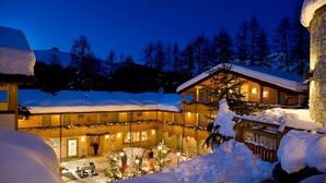A snow-covered lodge with multiple levels, a wooden exterior, and a lit interior. - Boscone Suite Hotel (Madesimo)