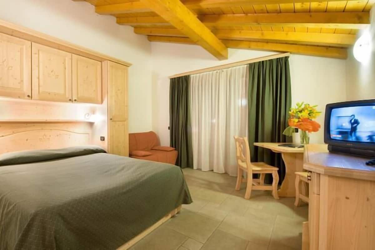 A hotel room with a bed, a desk with a chair, a television, and wooden cabinets.
