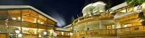 A multi-story wooden building with balconies, a stone dome, and snow-covered roofs. - Boscone Suite Hotel (Madesimo)
