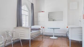 A room with two single beds, a small round table, a chair, and a window with curtains.