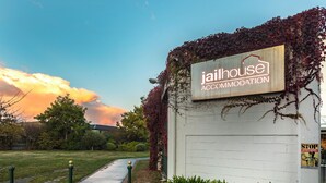 A sign for 'jailhouse accommodation' with a brick wall and greenery. - Jailhouse Accommodation - Hostel (Christchurch)