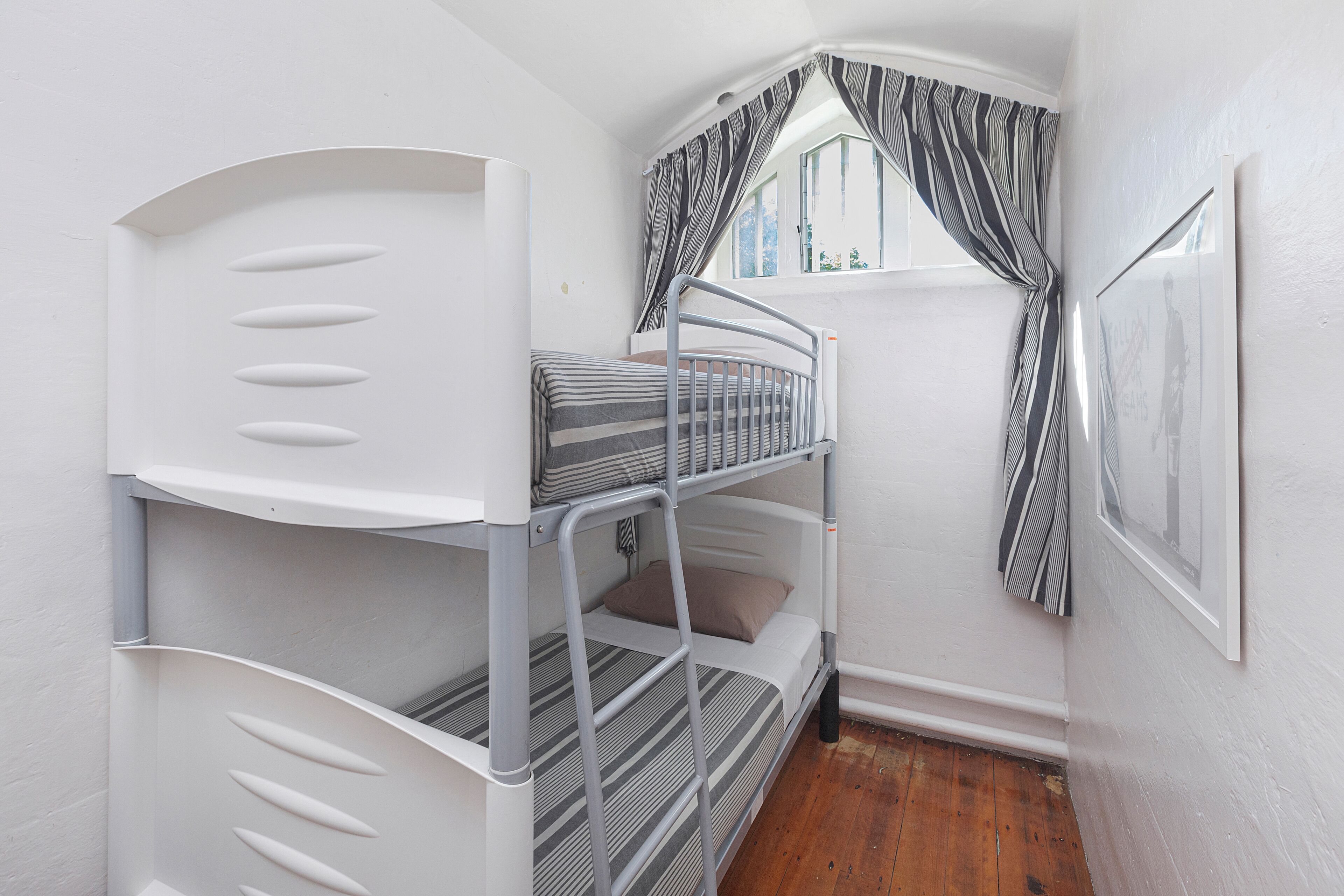Dormitorio con literas, ventana y cortinas, paredes blancas y suelo de madera.