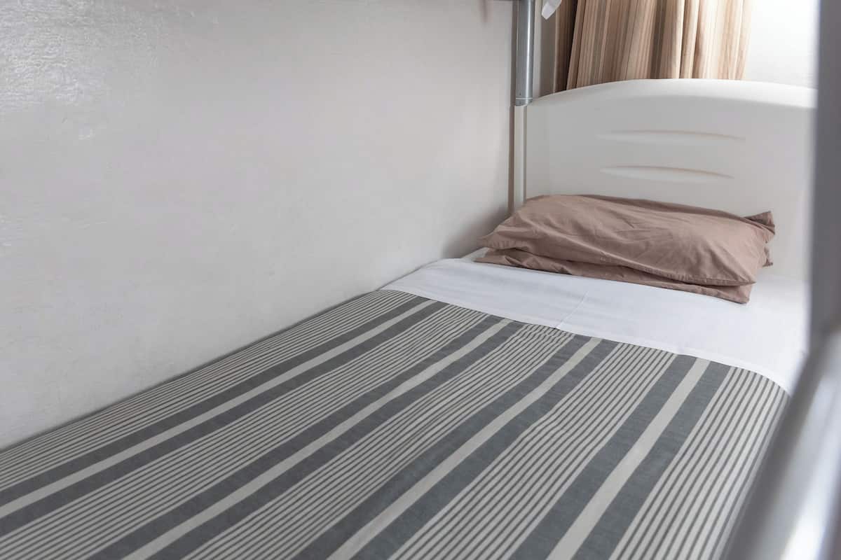 Una habitación pequeña con una cama individual, colcha a rayas, cabecera blanca y almohada color beige.