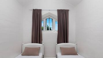 A room with two beds, a window with curtains, and a view of the sky.