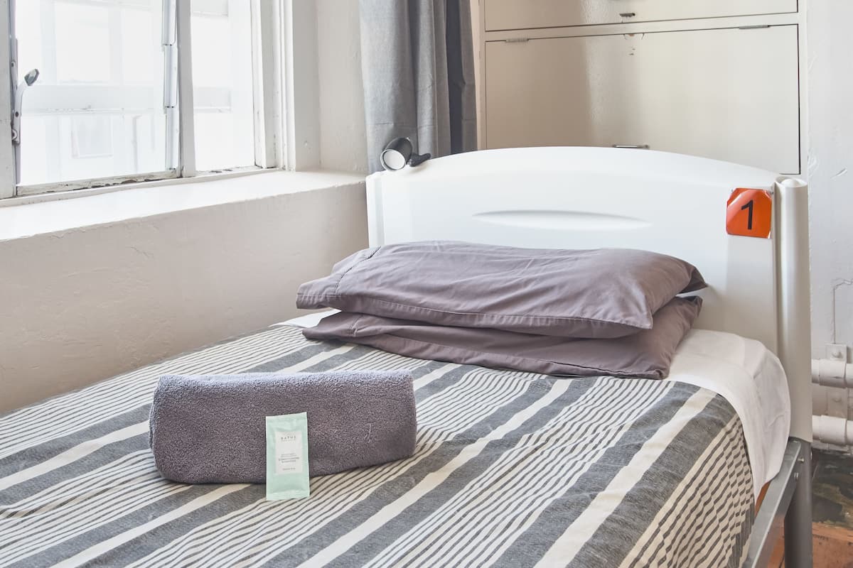 Una cama individual con una colcha a rayas, una almohada y una toalla enrollada.
