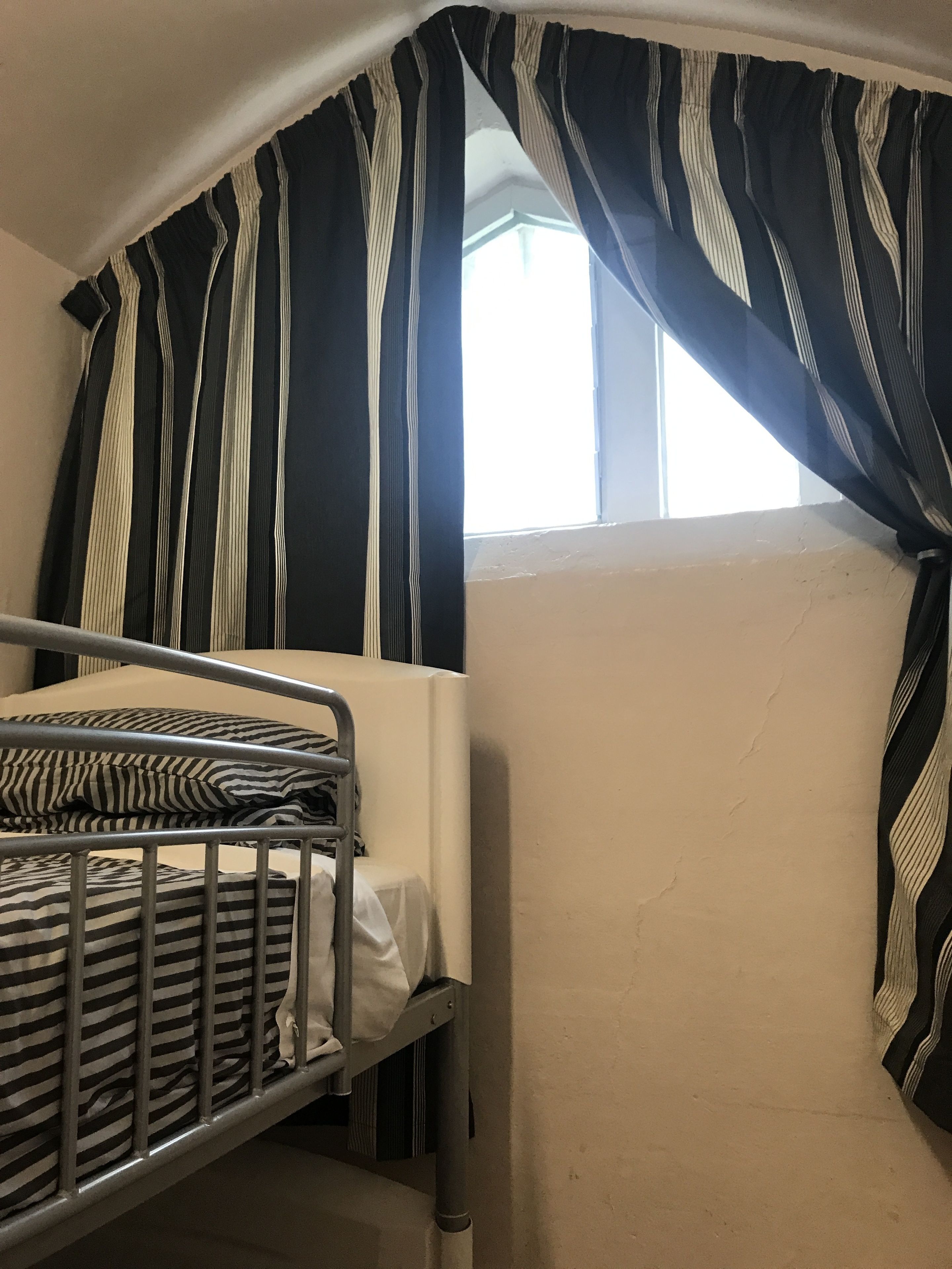 Un lit superposé dans une chambre avec une fenêtre, des rideaux à rayures et un mur uni.