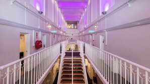 A hotel corridor with a central staircase, white railings, and purple lighting. - Jailhouse Accommodation - Hostel (Christchurch)