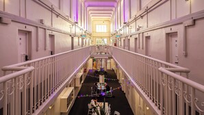 A hotel corridor with a central staircase, multiple doors, and a seating area with tables and chairs. - Jailhouse Accommodation - Hostel (Christchurch)