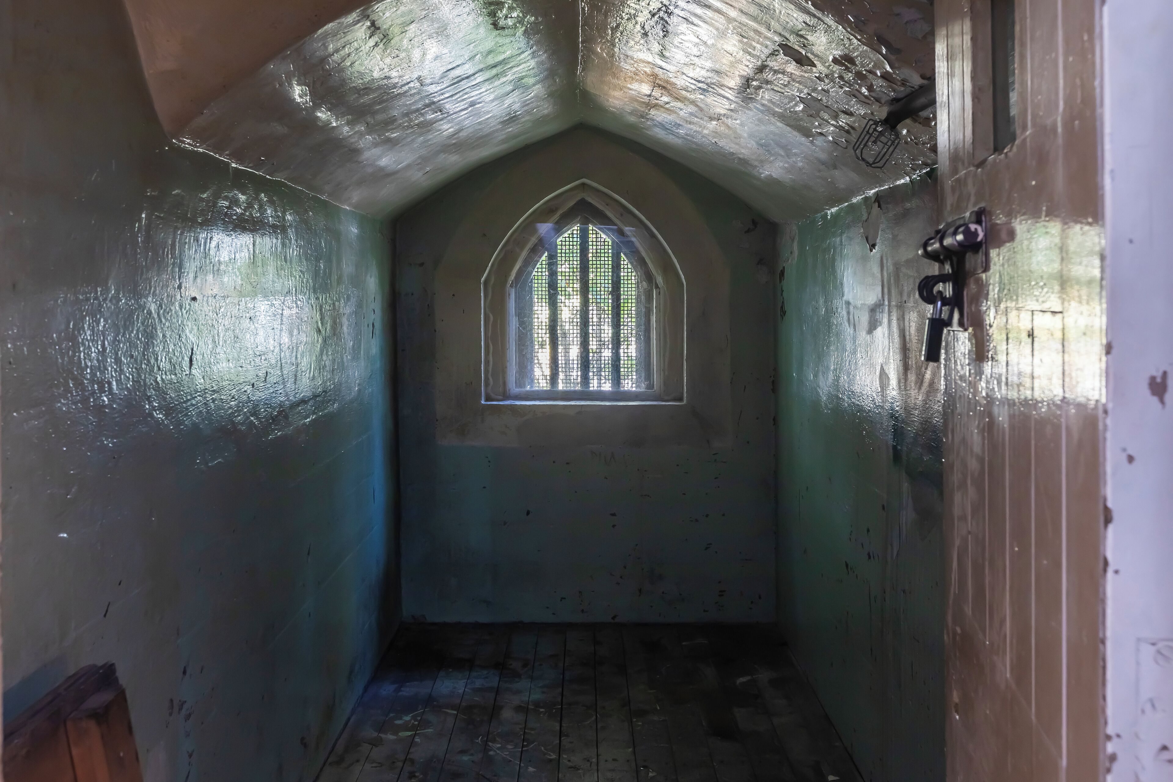 A narrow, dimly lit hallway with a small window at the end, wooden flooring, and a door on the right.