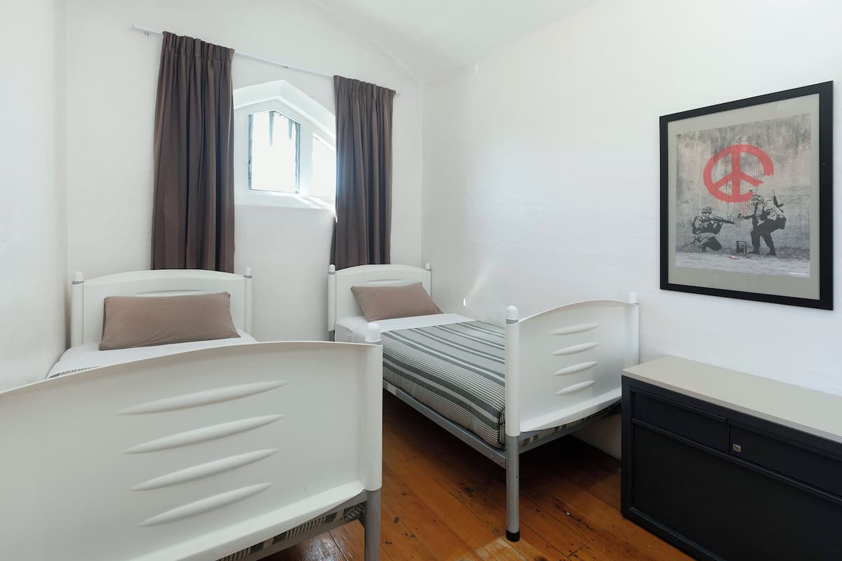Una habitación con dos camas individuales, una ventana con cortinas, una obra de arte enmarcada en la pared y un mueble auxiliar.