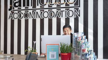 A reception desk with a computer, a phone, a QR code poster, a red potted plant, and a stack of brochures.
