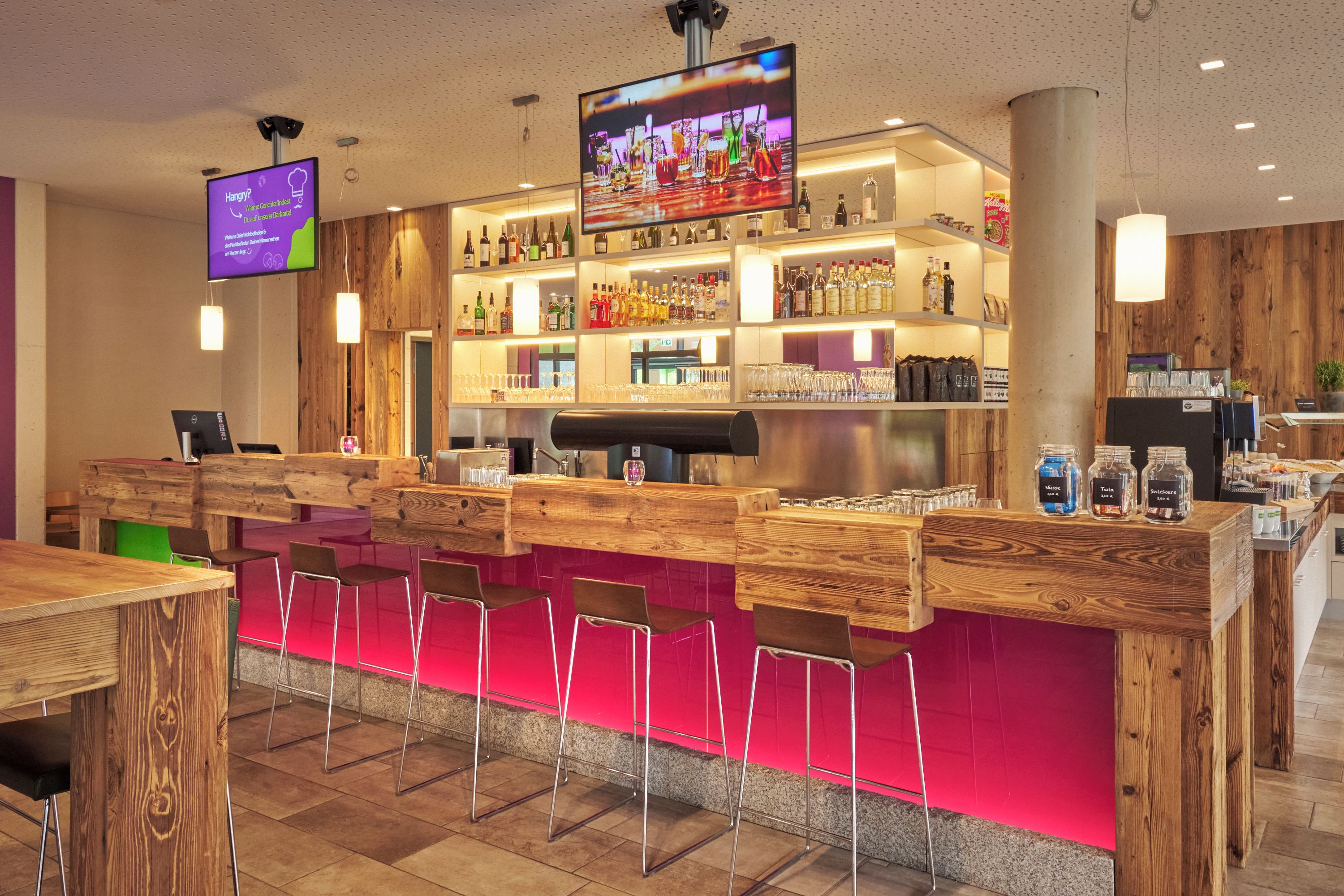 Zona de bar con mobiliario de madera, una pantalla de televisión y estantes llenos de botellas.
