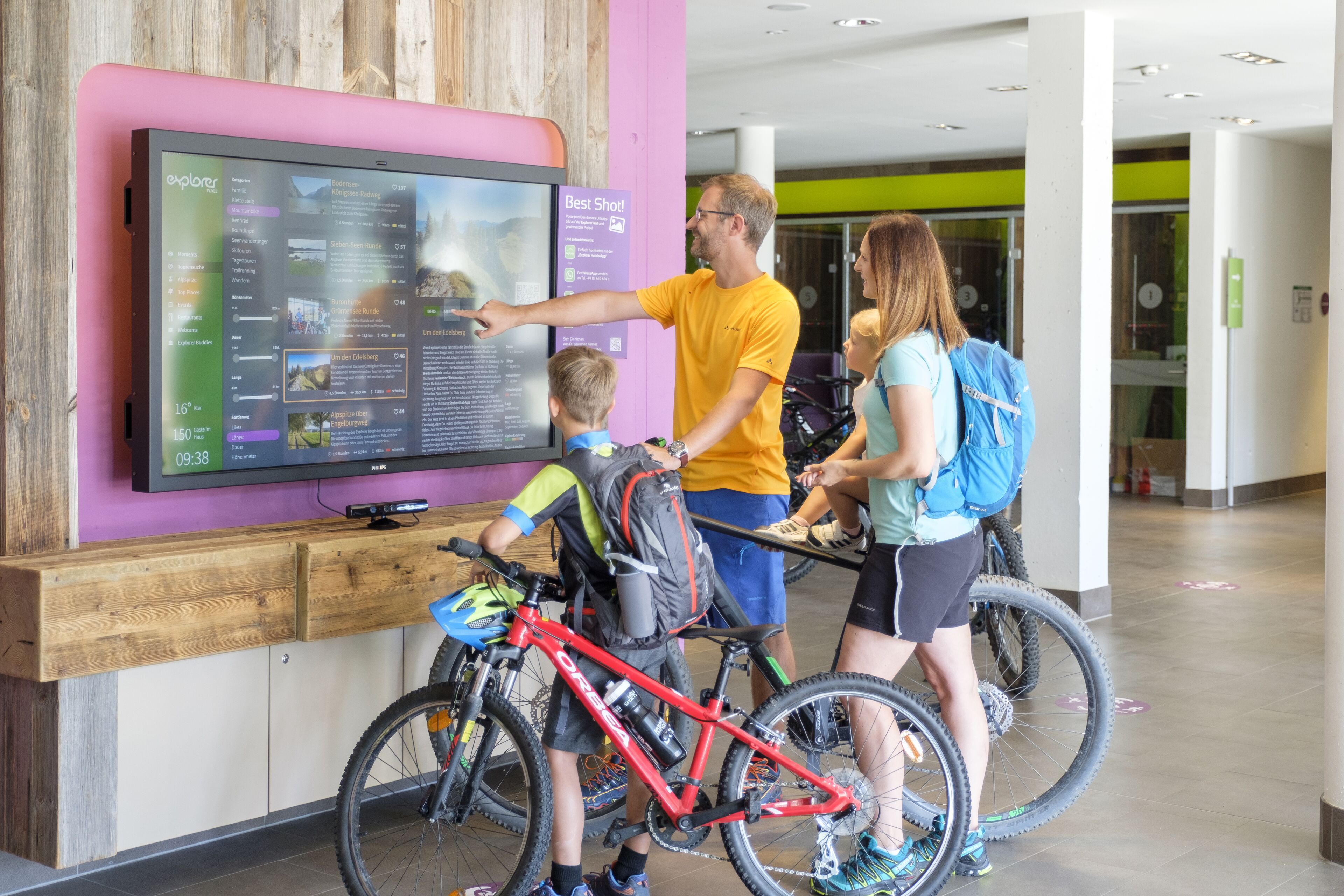 A family interacting with a digital display in a modern indoor setting, possibly a museum or information center.