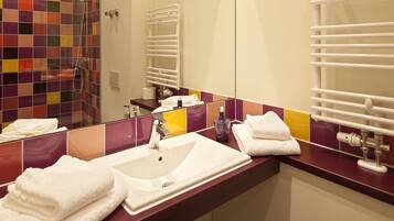Un baño con ducha de azulejos, lavamanos con espejo y un perchero para toallas.