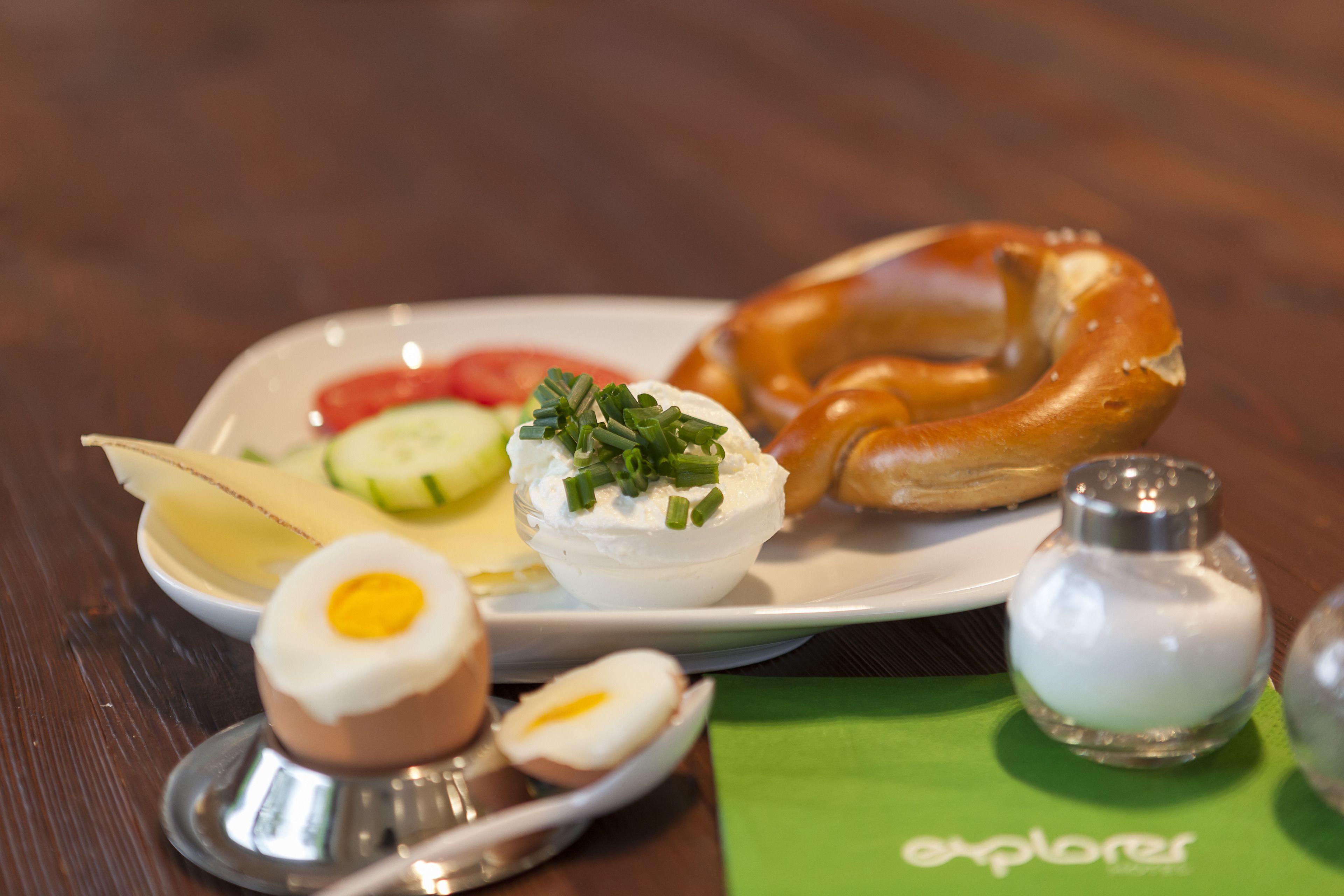 A plate with a pretzel, sliced vegetables, and a dollop of cream with herbs.