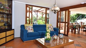 Una sala de estar con un sofá azul, una mesa de centro de vidrio y un comedor con muebles de madera.