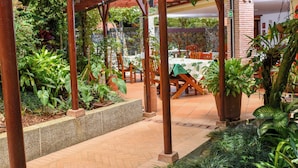 Un patio al aire libre con pérgolas de madera, plantas en macetas y una mesa lista para comer.