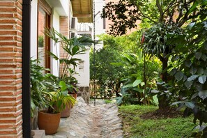 A stone pathway leading through a lush garden area with potted plants and a brick building. - La Campana Hotel Boutique (Medellín)