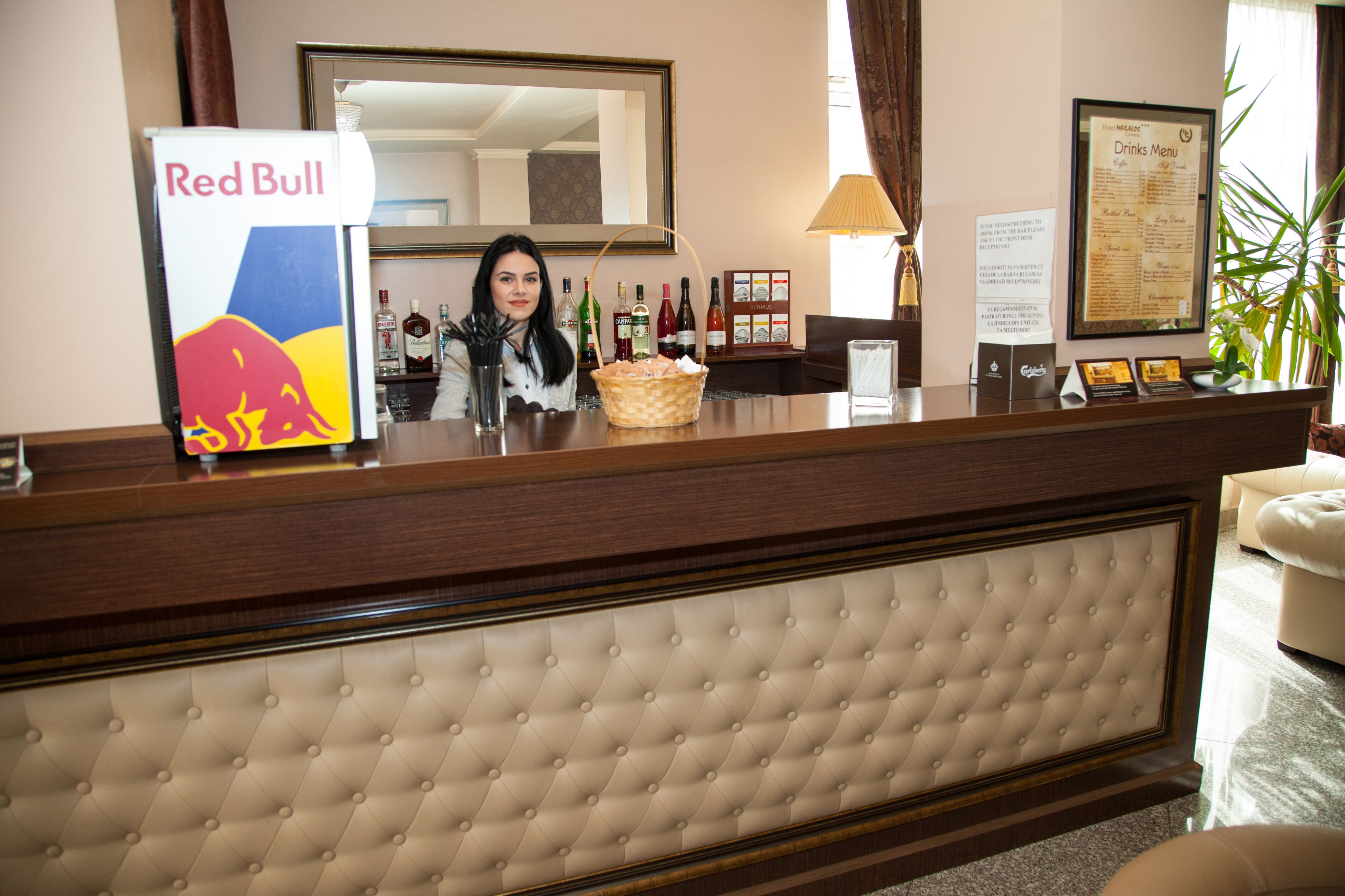 Zona de recepción de un hotel con un refrigerador de Red Bull, una carta de bebidas y un espejo sobre el mostrador.