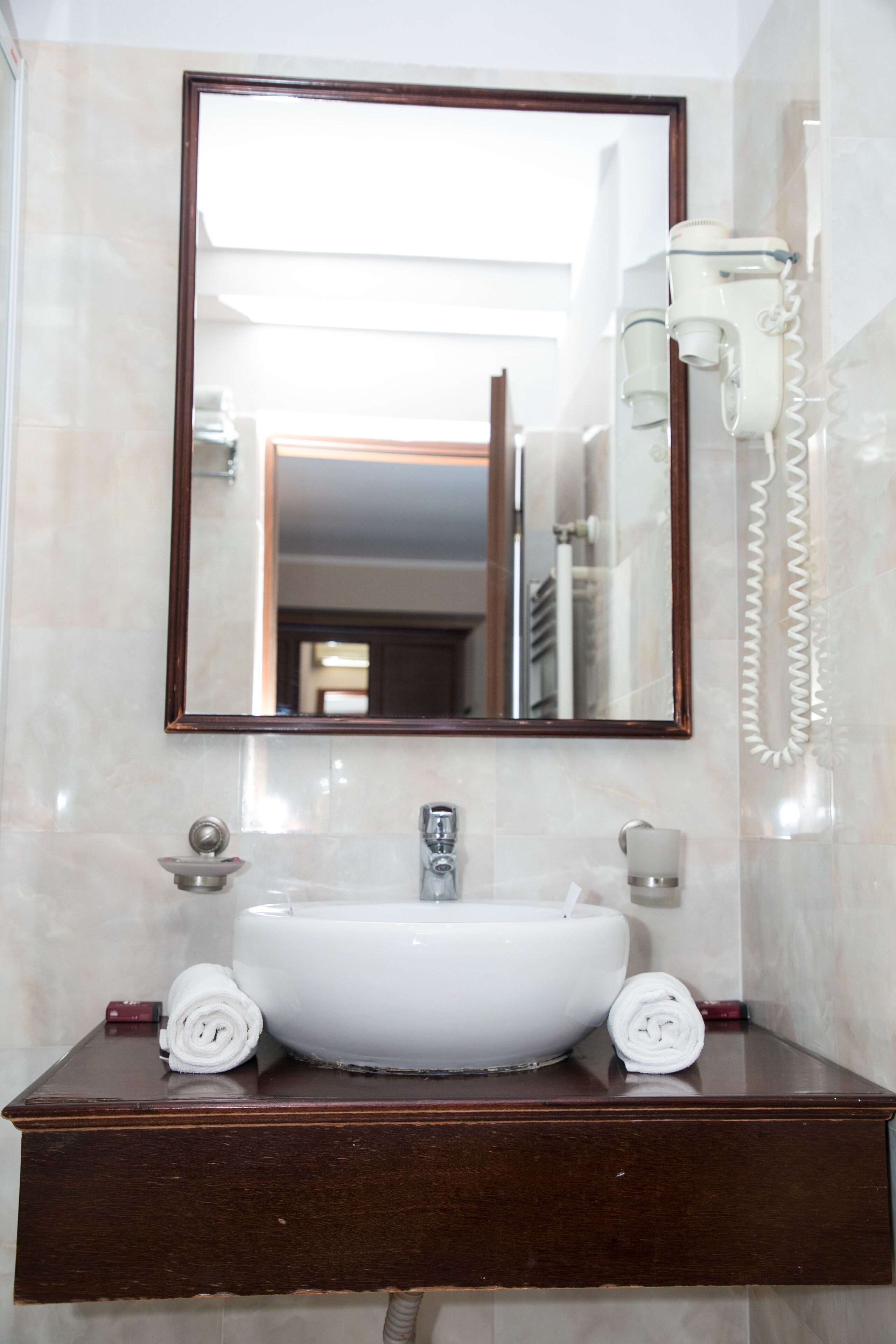 A bathroom with a white sink, a mirror, and a hairdryer mounted on the wall.