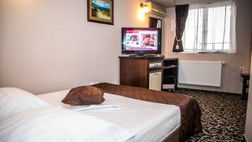 A hotel room with a bed, a television, a window with curtains, and a radiator.