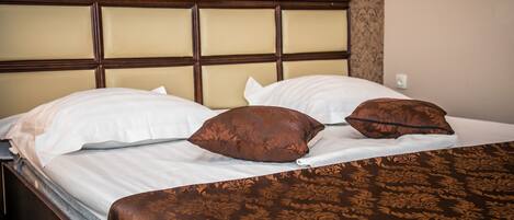 Una cama bien hecha con cabecera, dos almohadas blancas y dos almohadas decorativas marrones.