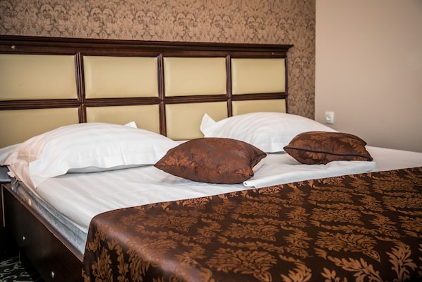 Cama bem arrumada com cabeceira, duas almofadas brancas e duas almofadas decorativas castanhas.