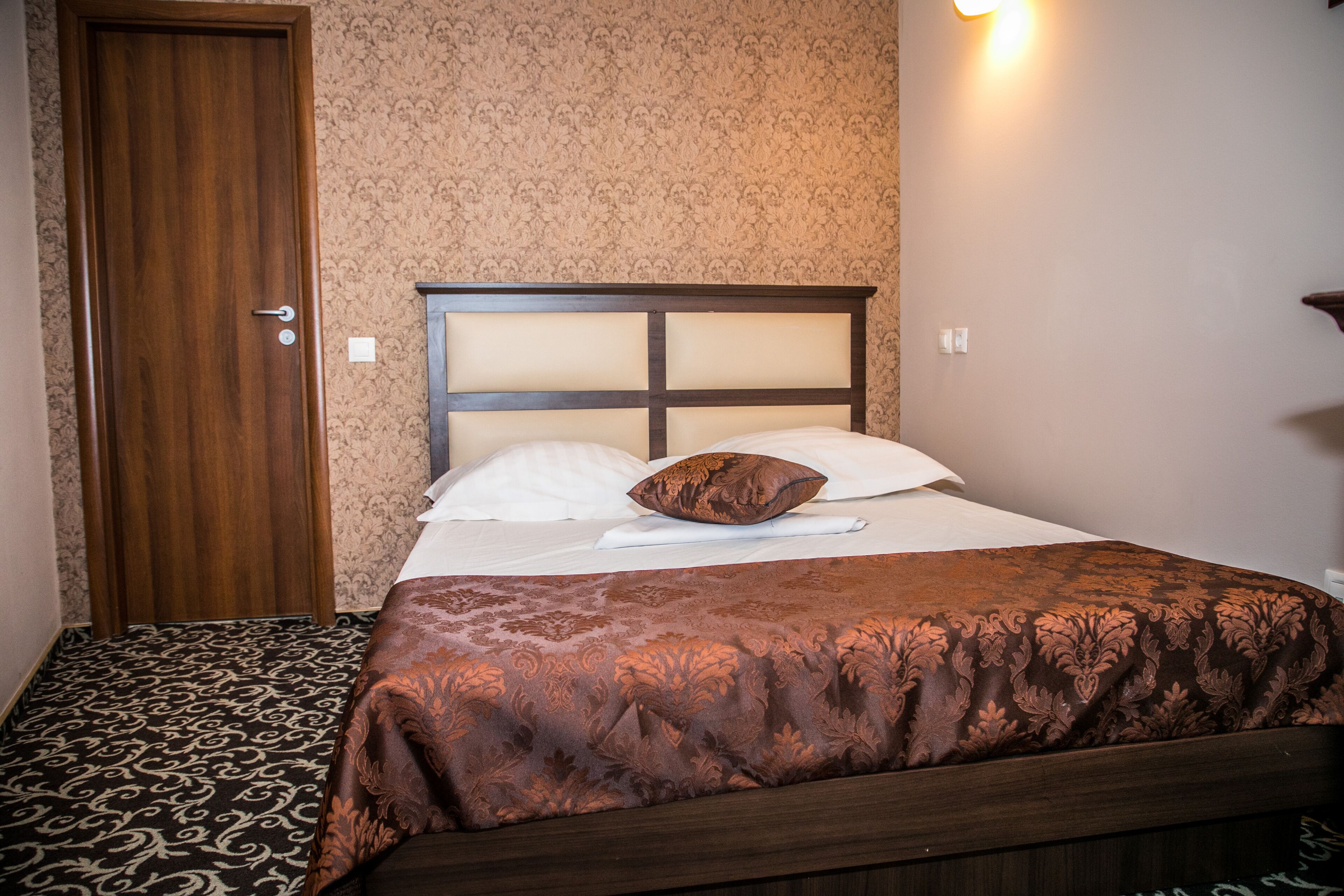 A neatly made bed with a headboard, a patterned carpet, and a wooden door.