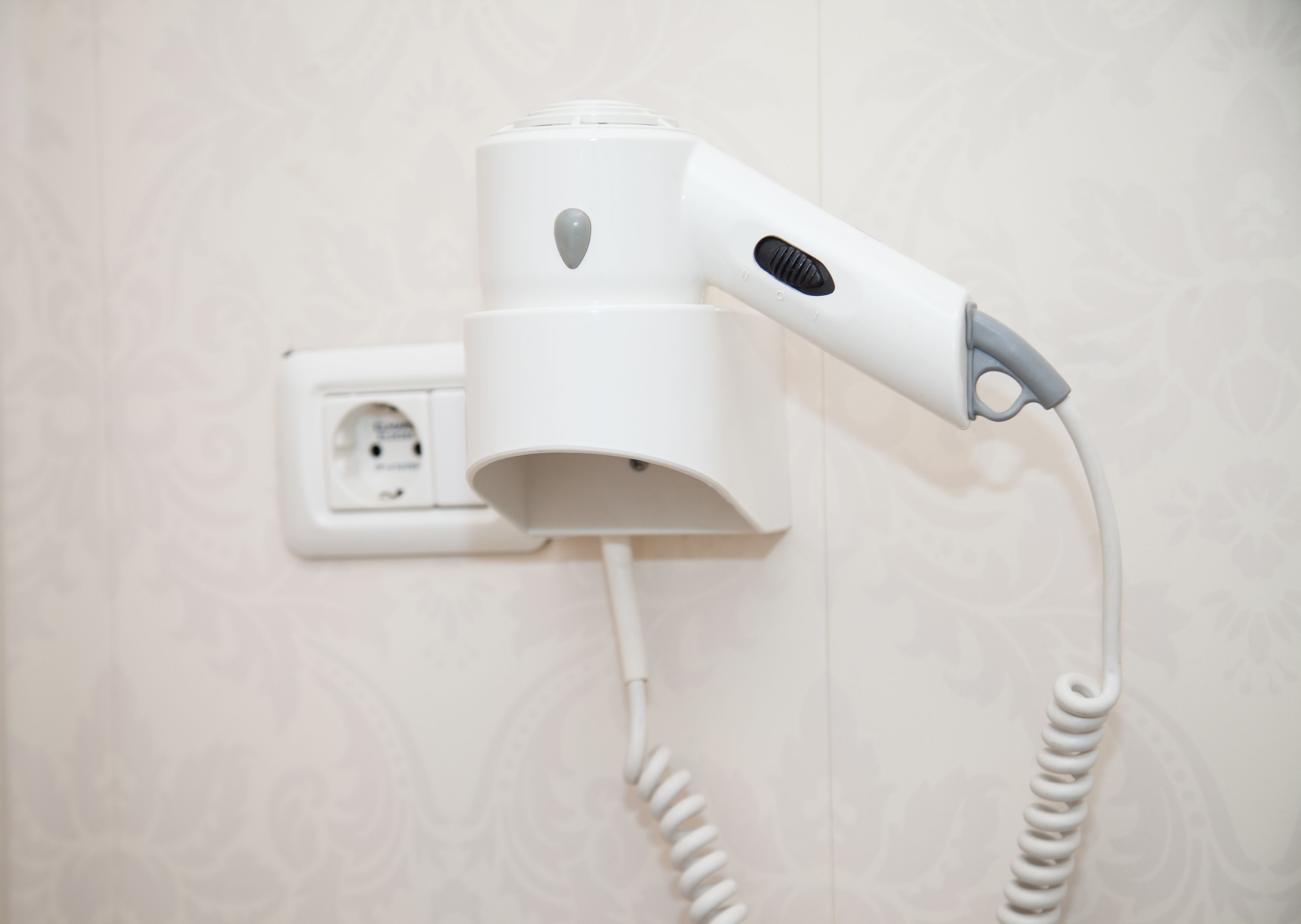 Un sèche-cheveux fixé au mur, à proximité d’une prise de courant.