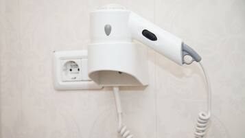 Un sèche-cheveux fixé au mur, à proximité d’une prise de courant.