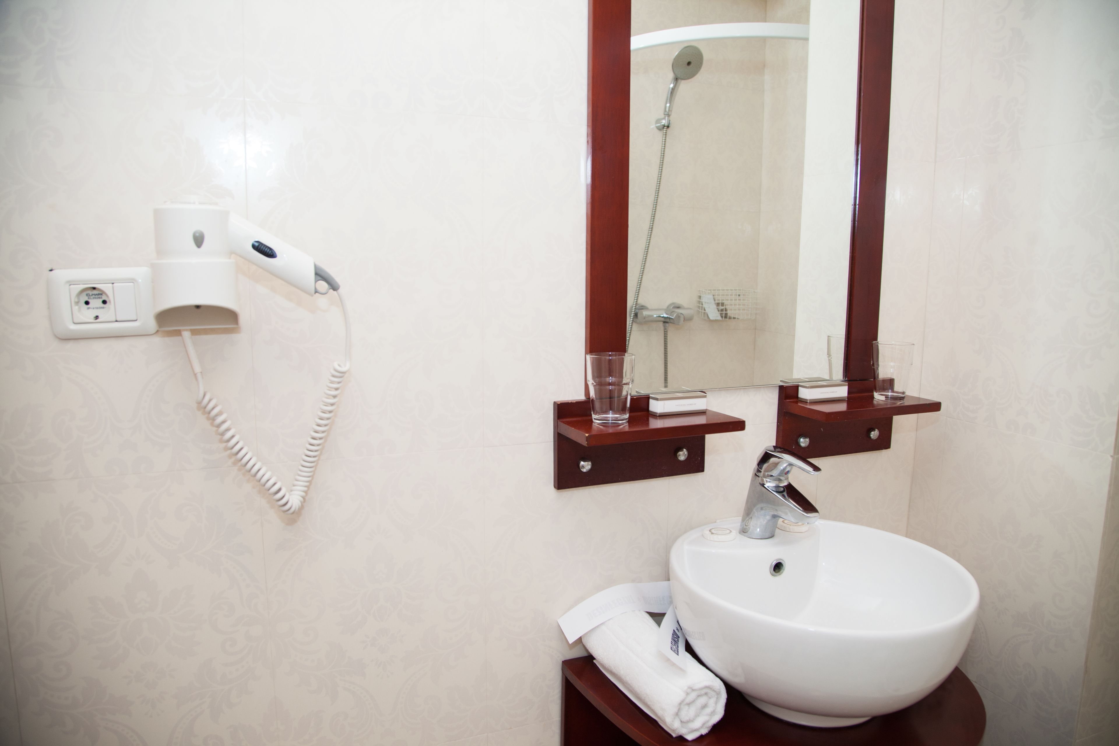 A bathroom with a white sink, a mirror, a towel, a hairdryer, and a shower.