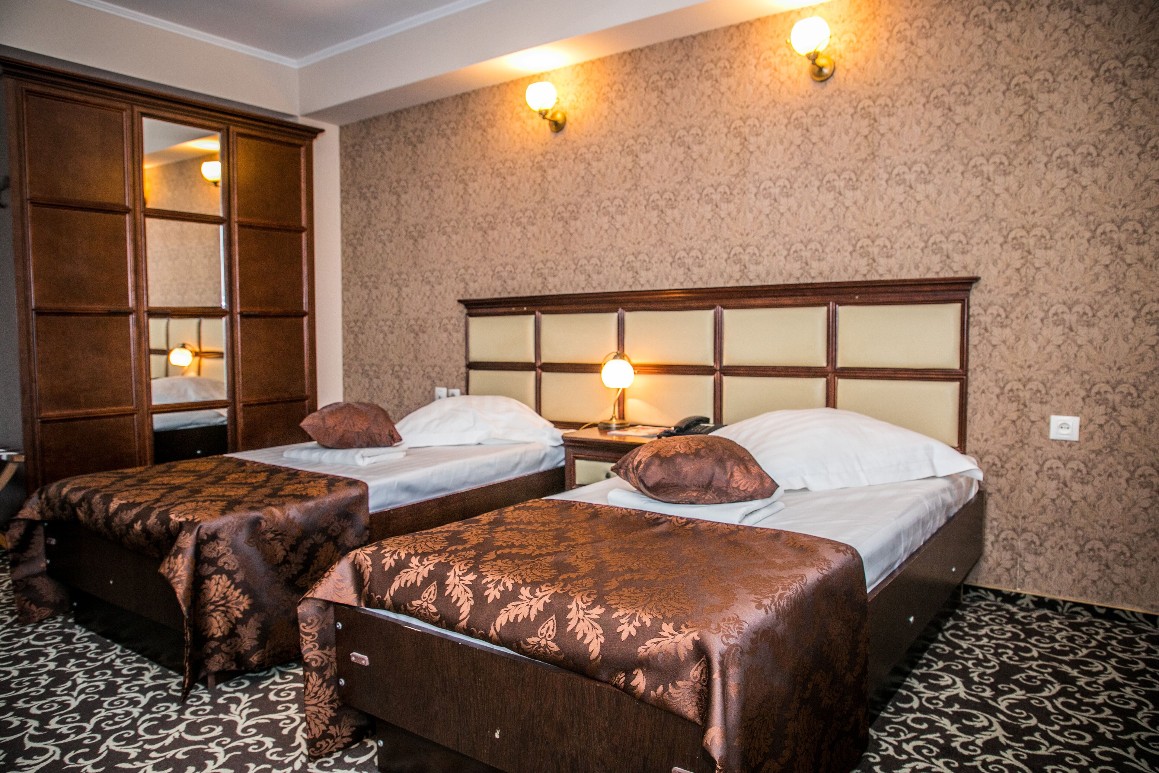 A hotel room with two beds, a wooden wardrobe, and a patterned carpet.