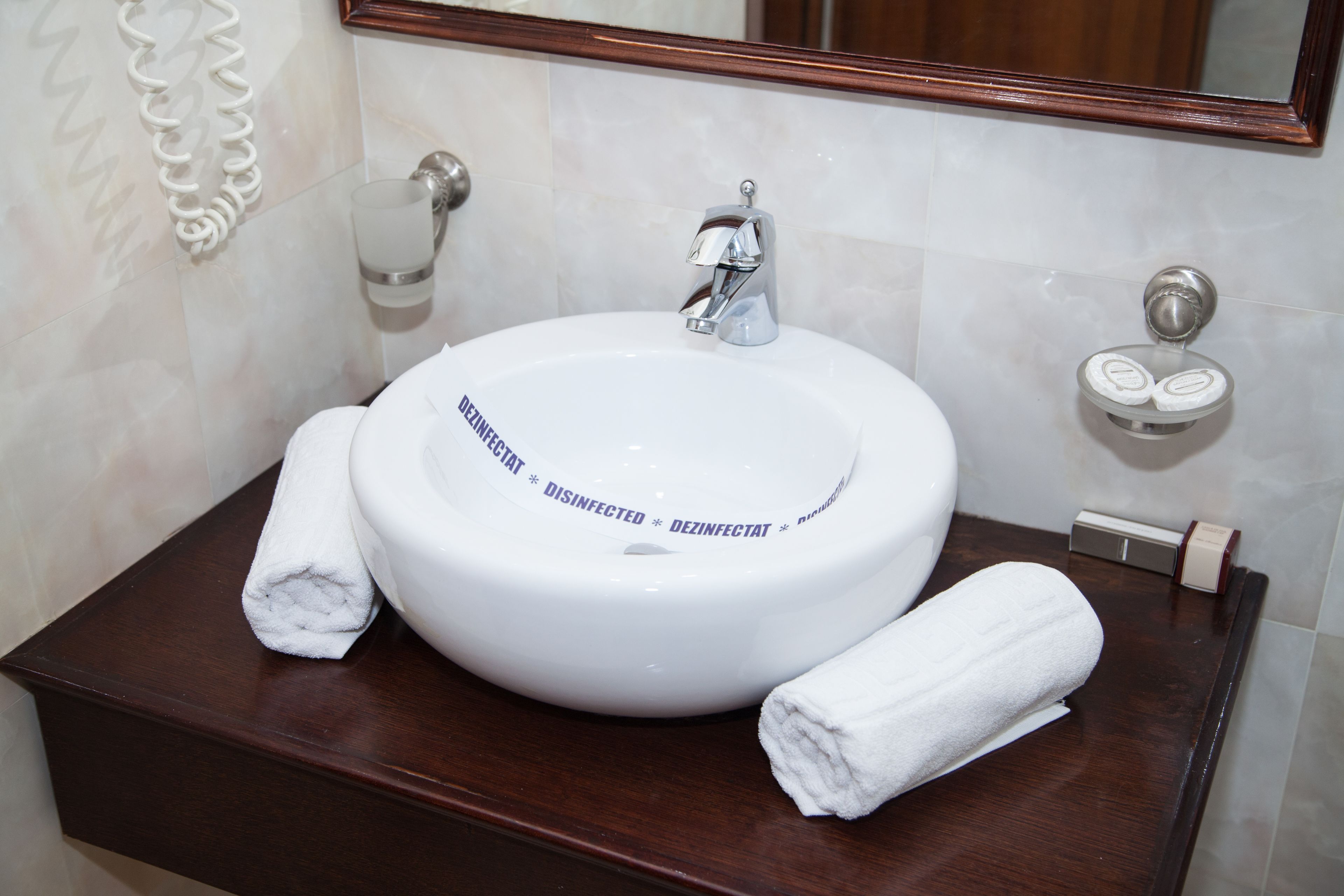 Un baño con un lavamanos blanco, un espejo y un perchero para toallas.