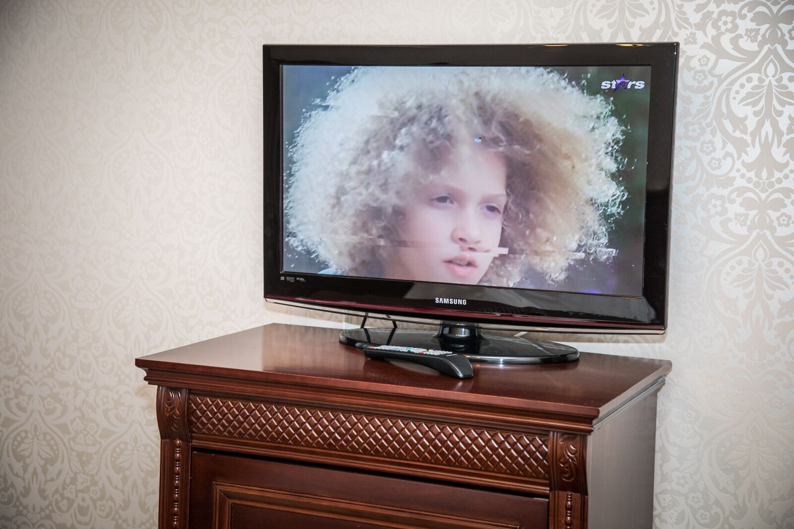 Un televisor sobre un mueble de madera, con un fondo de papel tapiz estampado.