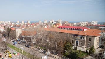 Un paisaje urbano con un edificio destacado que tiene techo rojo y varias ventanas, rodeado de otros edificios y un cielo despejado.