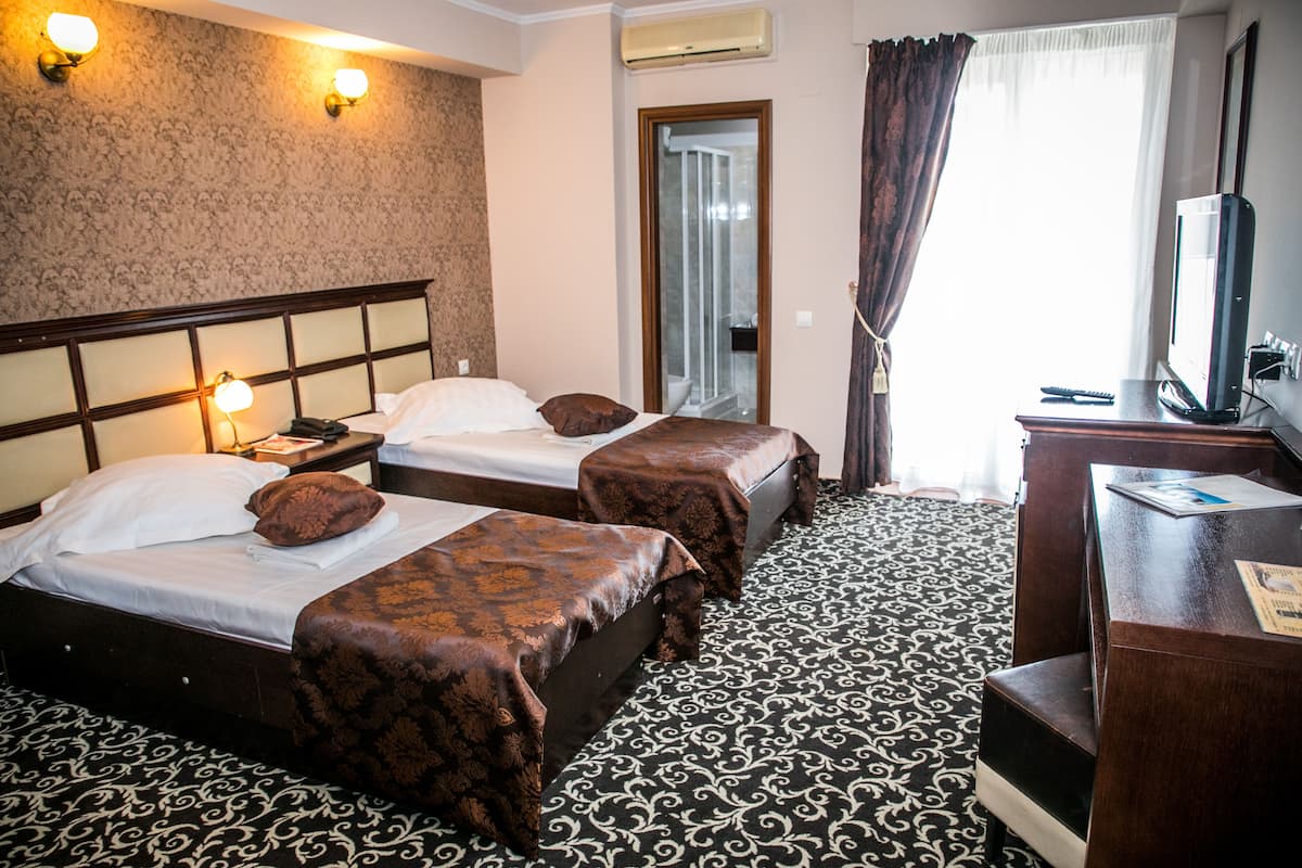 A hotel room with two beds, a desk, a TV, and a bathroom visible through a glass door.