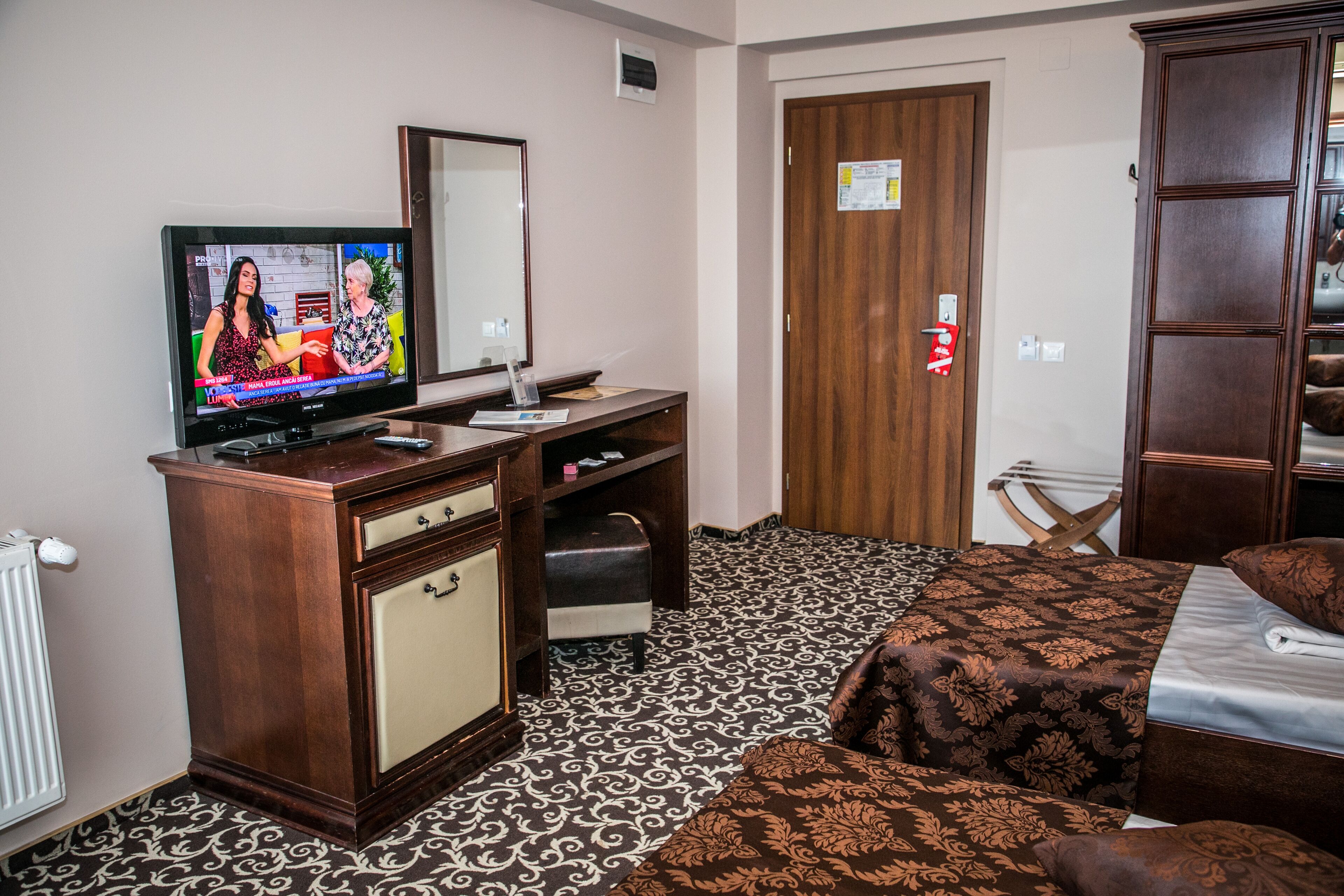 Habitación de hotel con una cama, un aparador de madera, un televisor y una puerta con picaporte rojo.