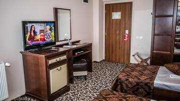 Habitación de hotel con una cama, un aparador de madera, un televisor y una puerta con picaporte rojo.