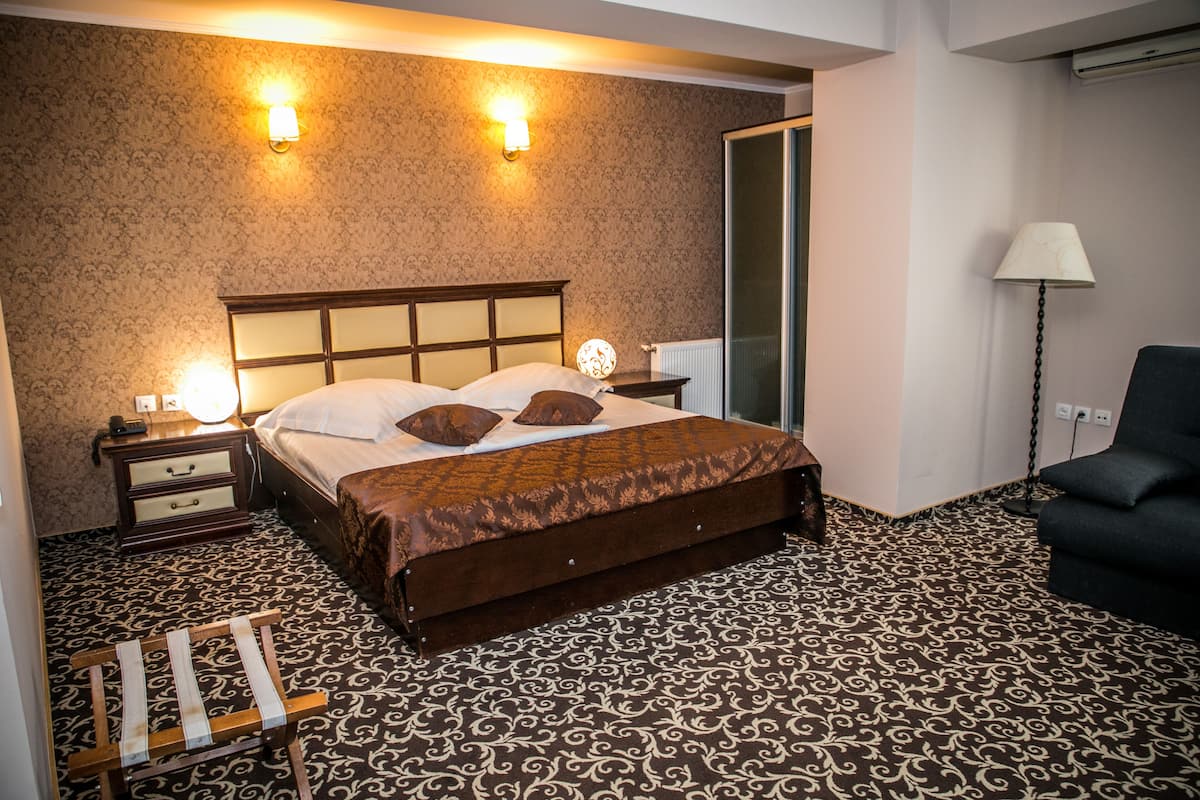 A hotel room with a large bed, two bedside lamps, a nightstand, a chair, and a mirror.