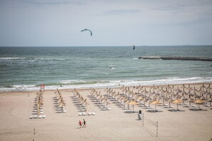 A beach with rows of sun loungers and umbrellas, a rocky breakwater, and a view of the sea. - Hotel Megalos (Constanta)